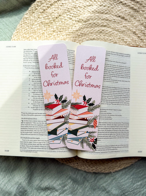 Christmas-themed pun "All Booked for Christmas" bookmarks on an open book with a textured surface in the background.