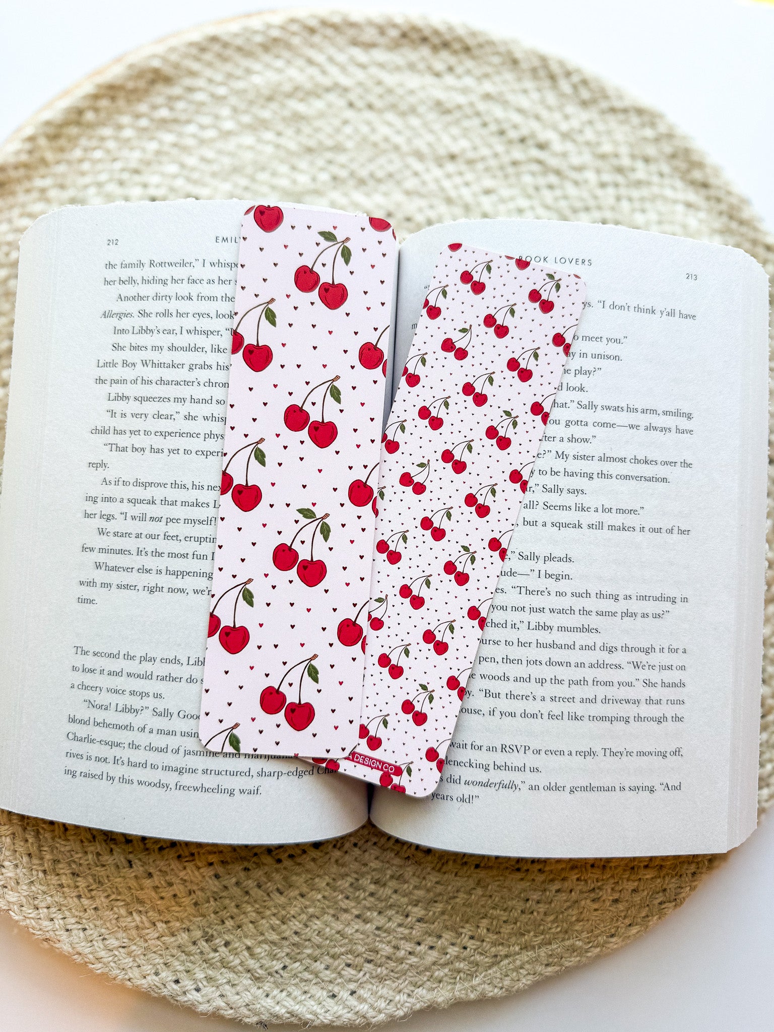 Open book with a cherry-patterned bookmark on a woven surface