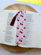Open book with a cherry-themed bookmarkwith dark red tassel on a wooden surface
