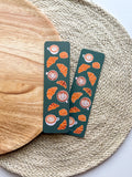 Two green bookmarks with croissant and coffee pattern on a woven mat