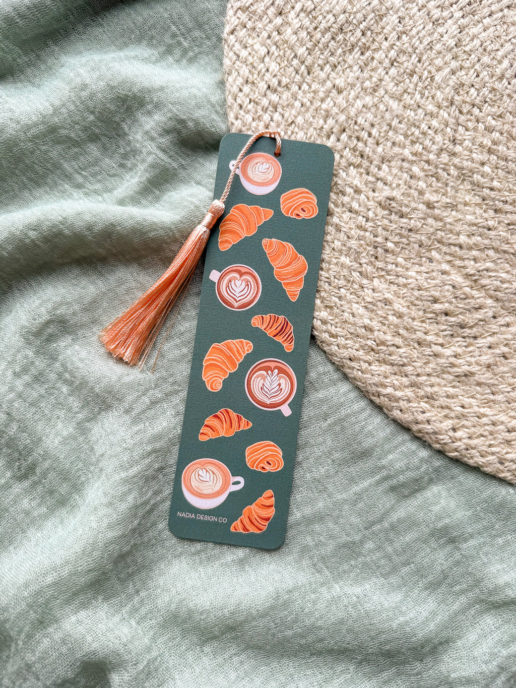Bookmark with croissant and coffee design with a tassel on a textured fabric background