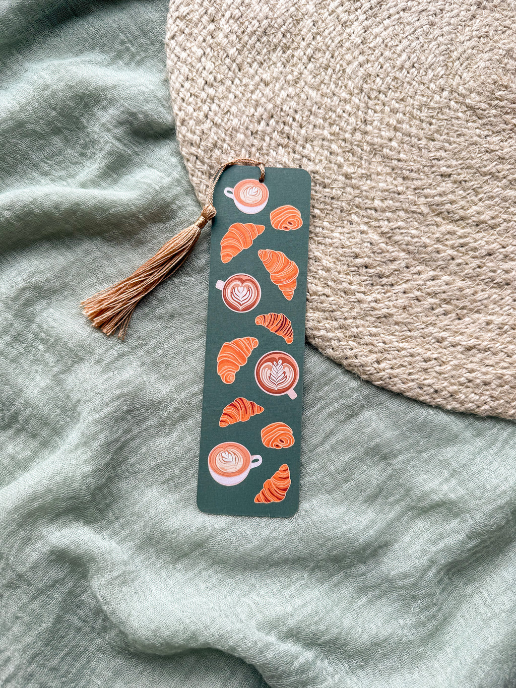 Bookmark with coffee and croissant designs with tassel on a textured fabric background