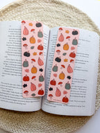 Open book with two bookmarks featuring autumn-themed illustrations on a woven surface.