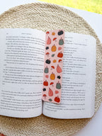 Open book with a colorful bookmark featuring pumpkins and leaves on a textured surface.