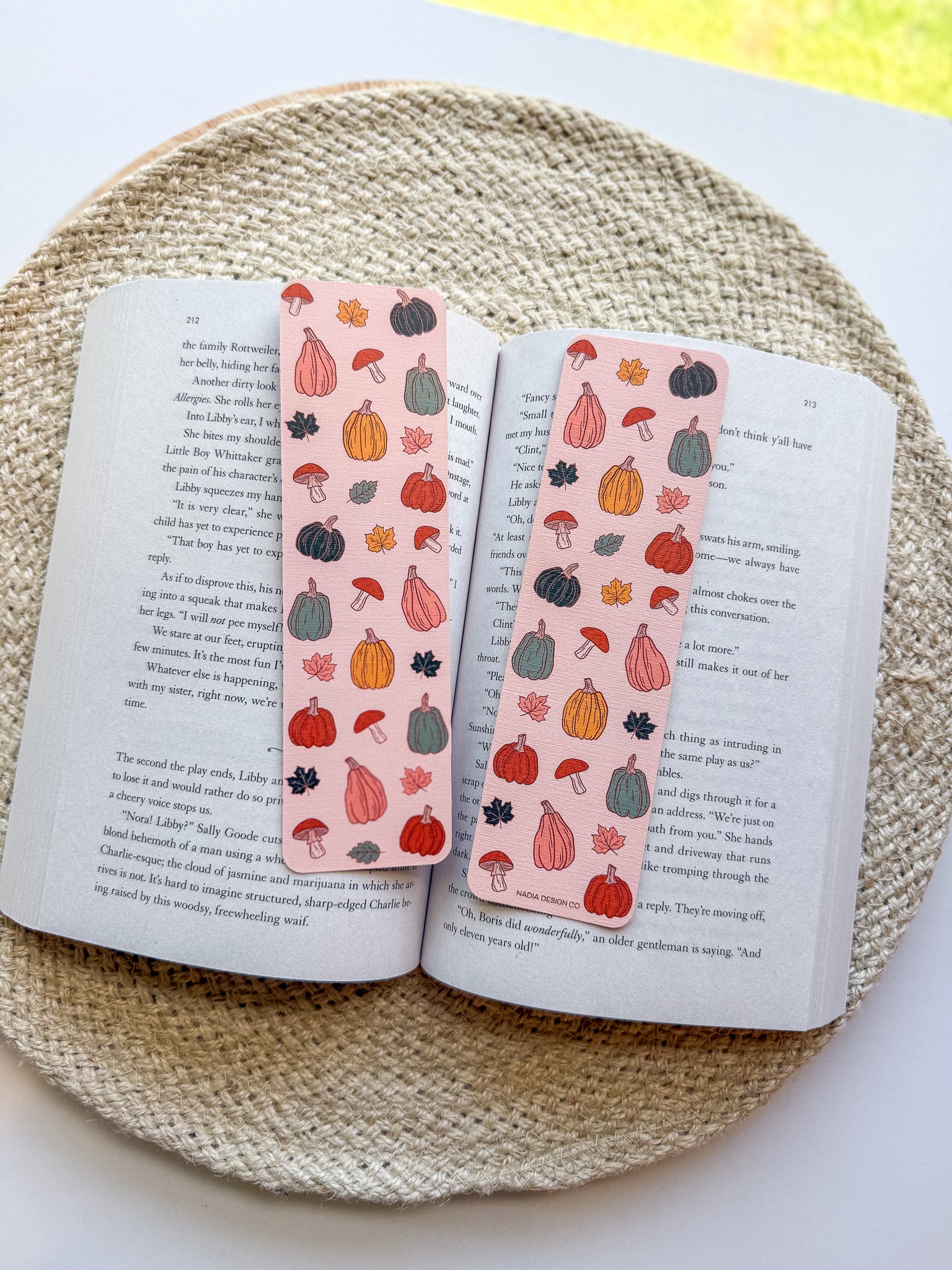 Open book with decorative bookmarks featuring pumpkins and mushrooms on a woven surface.