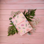 A greeting card with a floral birthday bouquet illustration and the text 'Happy Birthday!' on the front, accompanied by a white envelope, against a pink background.