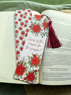poinsettia Floral Christian bookmark with text" Jesus is the reason for the season" with dark red tassel on a textured surface