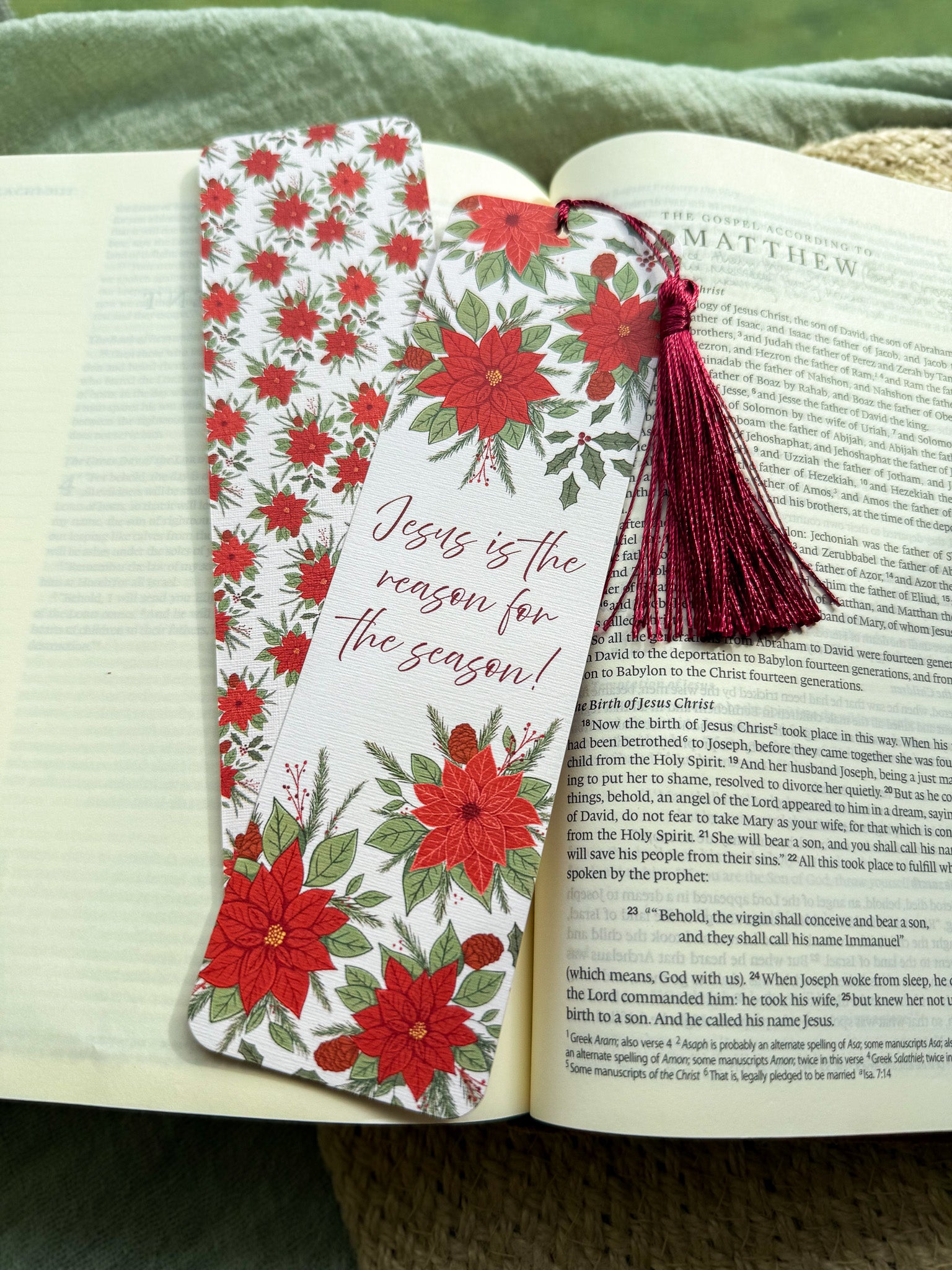 poinsettia Floral Christian bookmark with text" Jesus is the reason for the season" with dark red tassel on a textured surface