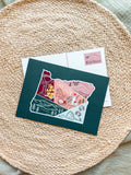 Postcard with a colorful illustration of Oregon held by a hand on a textured surface.