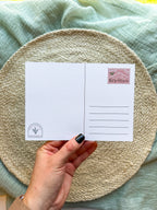 back of postcard with a colorful illustration of Oregon held by a hand on a textured surface.