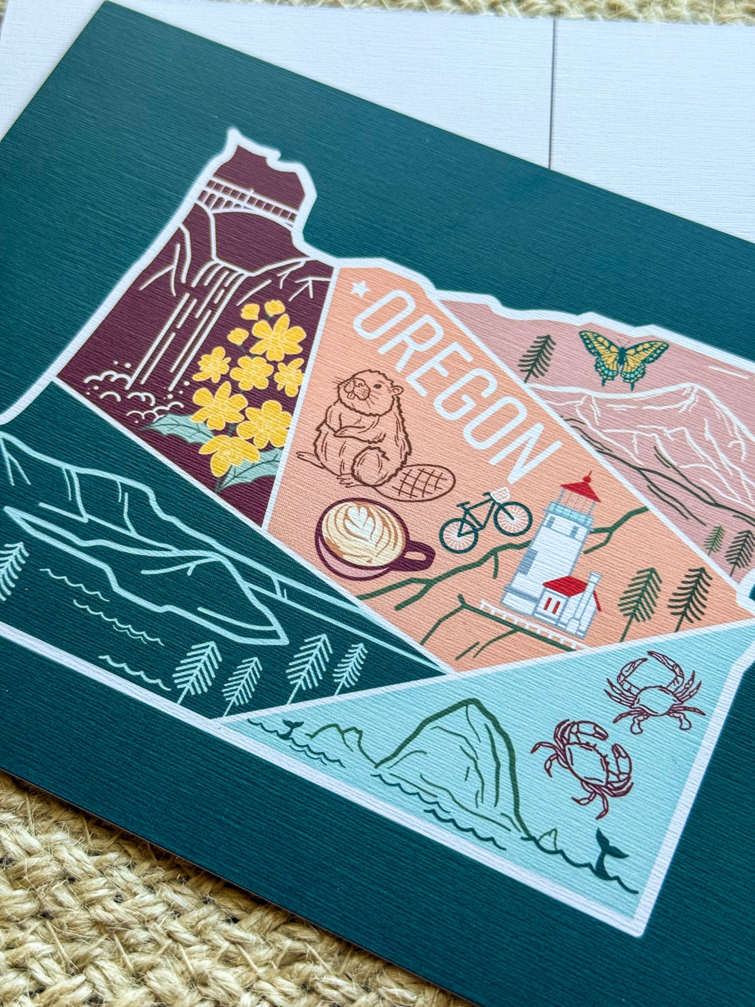 Postcard with a colorful illustration of Oregon held by a hand on a textured surface.
