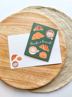 Greeting card "thanks a brucnh" pun with croissant and coffee illustrations on a wooden plate