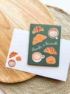Greeting card "thanks a brunch" pun with croissant and coffee illustrations on a wooden background
