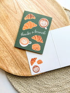 Greeting card "thanks a brunch" pun with croissant and coffee illustrations on a wooden background