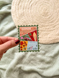 Colorful Vermont-themed stamp magnet held by a hand on a textured fabric background