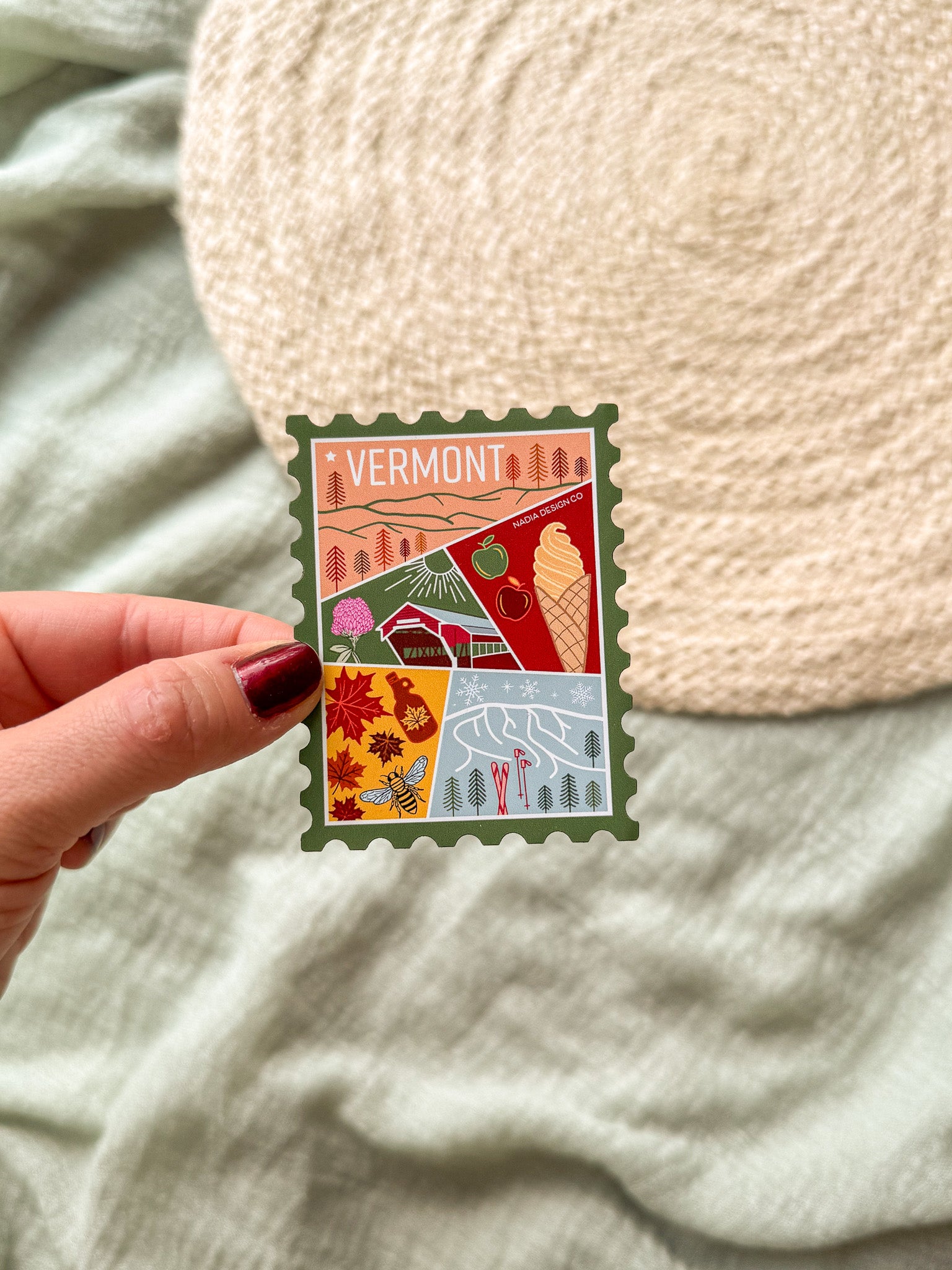 Colorful Vermont-themed stamp magnet held by a hand on a textured fabric background