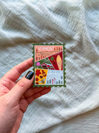 Colorful Vermont-themed stamp magnet held by a hand on a textured fabric background