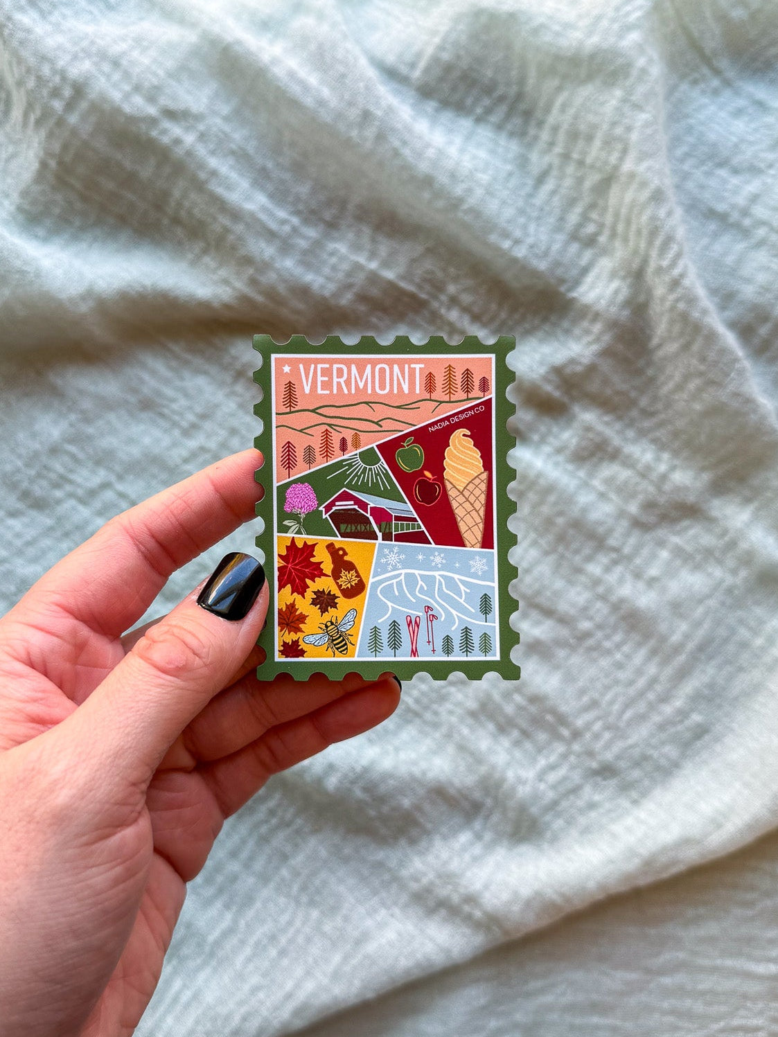 Colorful Vermont-themed stamp magnet held by a hand on a textured fabric background