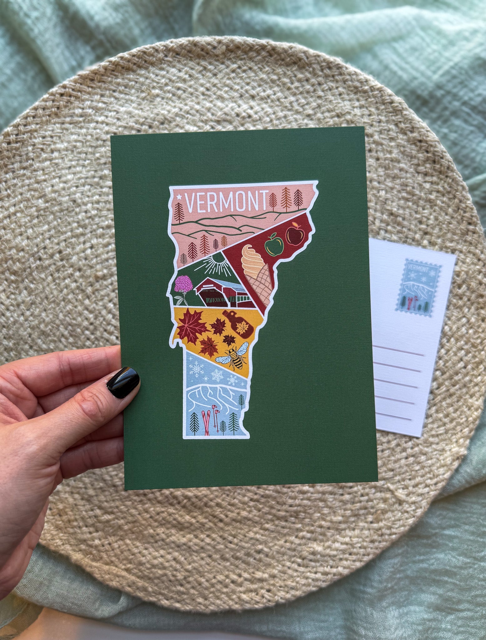 Postcard with a colorful illustration of Vermont held by a hand on a textured surface.