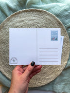 back Postcard with a colorful illustration of Vermont held by a hand on a textured surface.