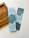 A bookmark featuring a blue background with clouds, the sun, and a cross, along with the Bible verse Psalm 46:10.