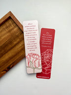 A bookmark with a rose illustration and a red tassel, placed on an open book.
