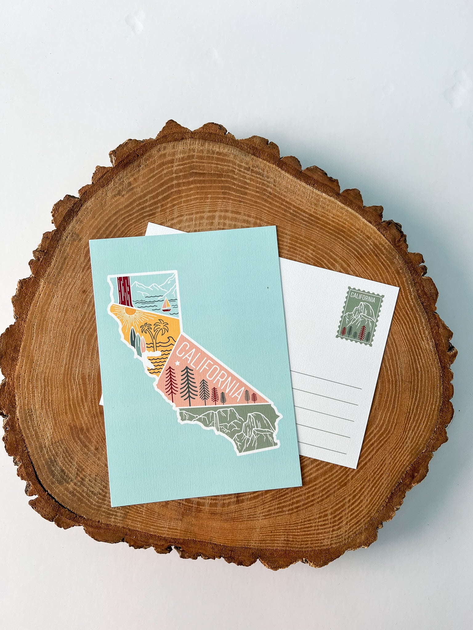 A colorful postcard featuring an illustration of California's landscape, including mountains, a beach, and iconic symbols like palm trees and a sailboat.