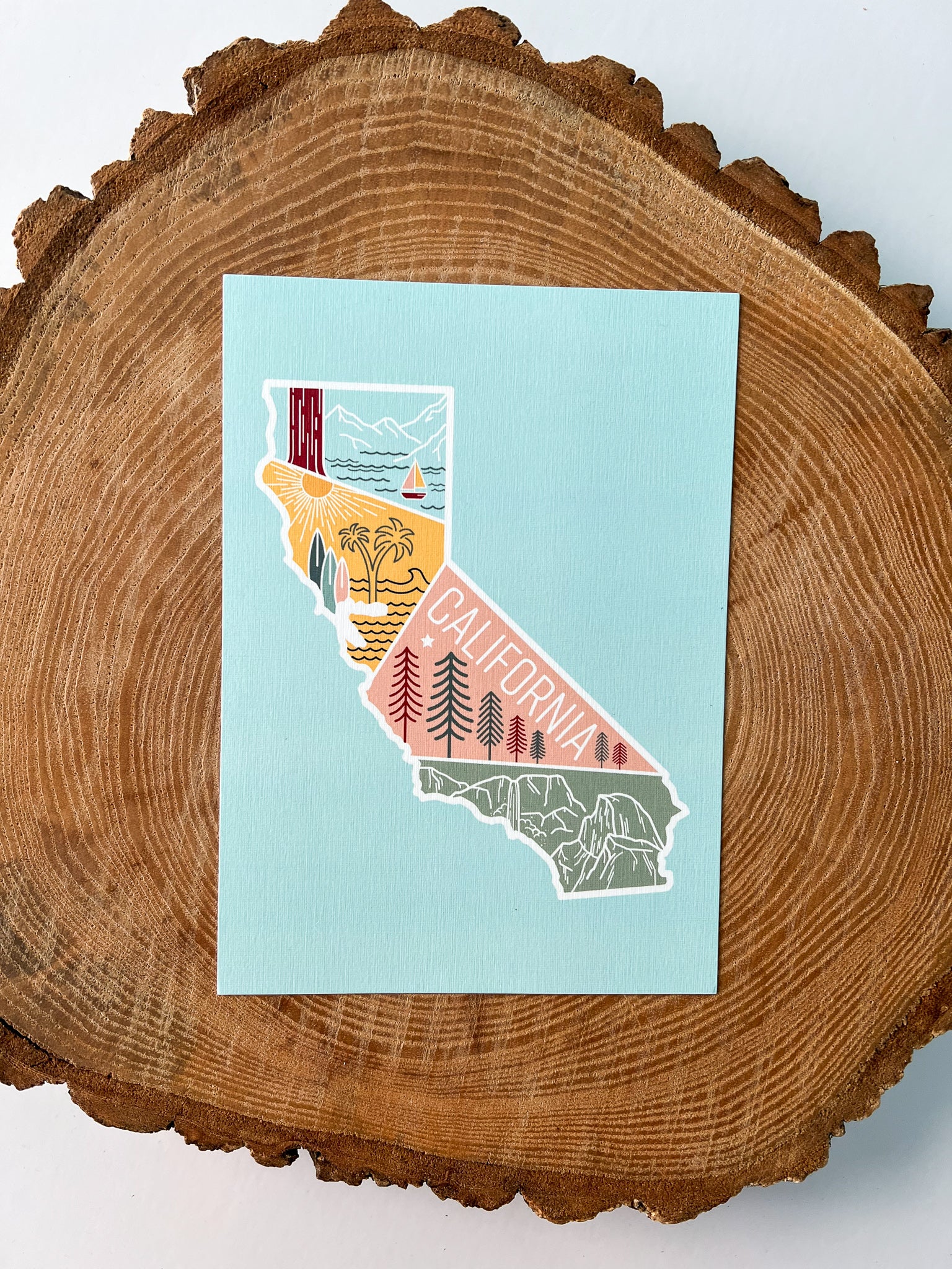 A colorful postcard featuring an illustration of California's landscape, including mountains, a beach, and iconic symbols like palm trees and a sailboat.