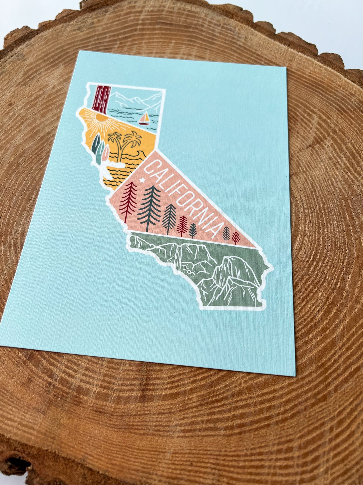A colorful postcard featuring an illustration of California's landscape, including mountains, a beach, and iconic symbols like palm trees and a sailboat.