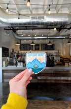 A vinyl sticker with an illustration of a cabin in a mountainous landscape with the text 'EXPLORE MORE' 