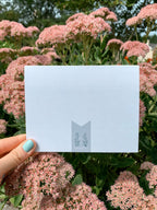 background of greeting card with illustrations of three cacti in pots and the text 'HOPE YOUR BIRTHDAY IS ON POINT!' on it, placed on a wooden surface with leaves around.