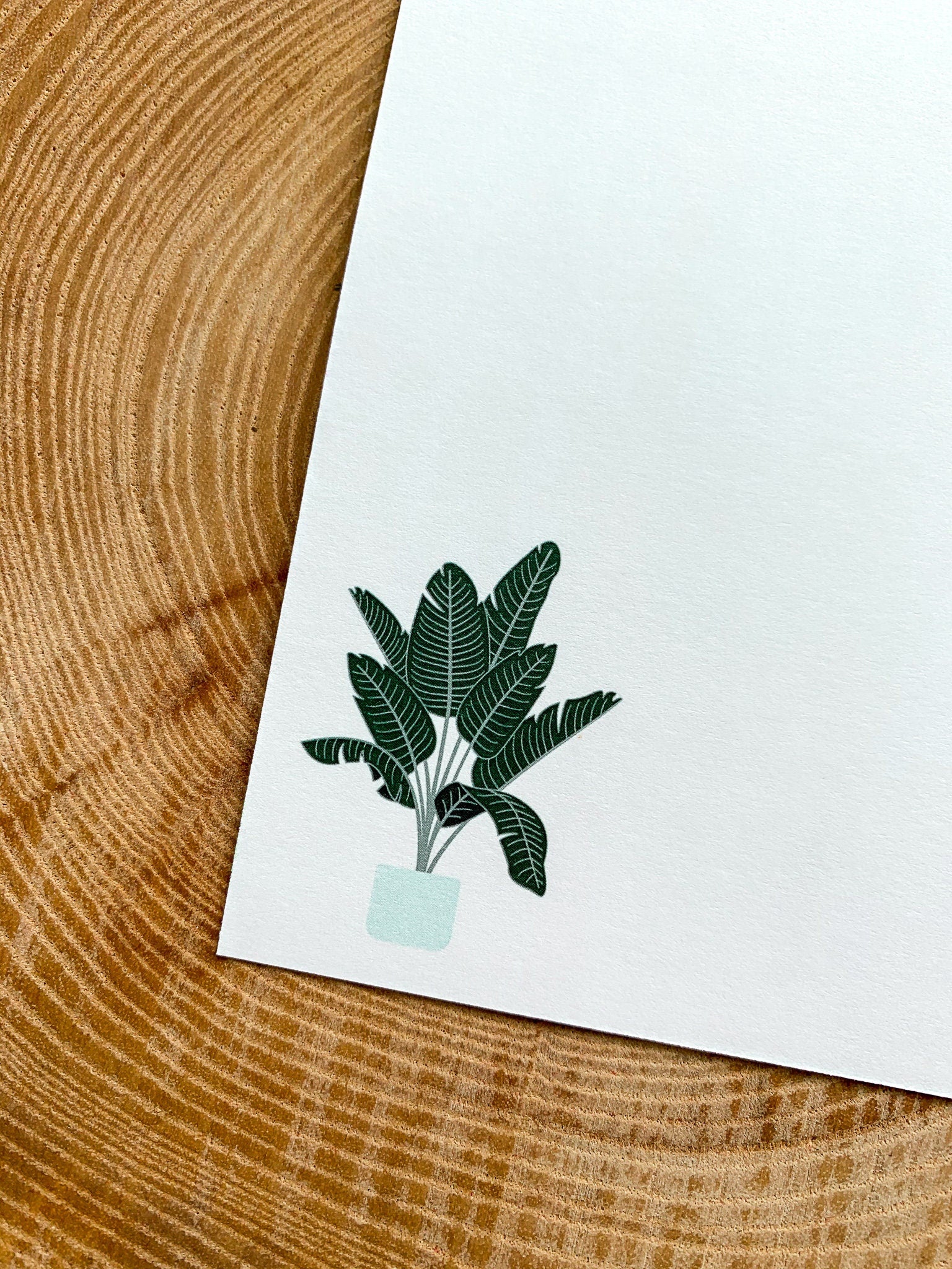 A greeting card with a plant illustration ' on it, placed on a wooden surface with some leaves beside it.