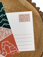 A postcard featuring a colorful illustration of Utah's landscape, including mountains and trees, with the word 'UTAH' prominently displayed.