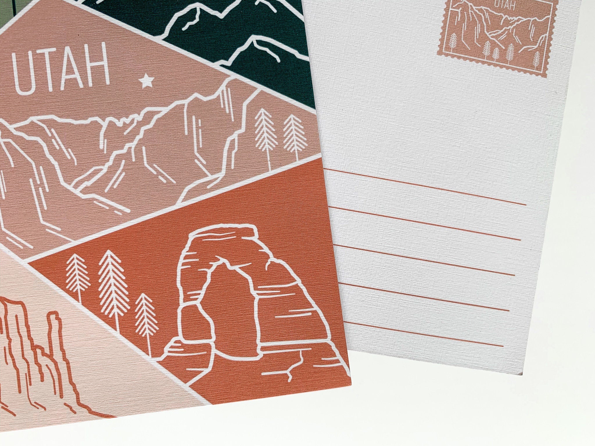 A postcard featuring a colorful illustration of Utah's landscape, including mountains and trees, with the word 'UTAH' prominently displayed.