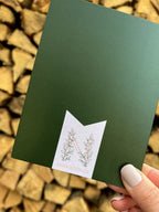 A hand holding a Christmas card with 'Peace on Earth' written on it, featuring a green background, a red bow, and stars.