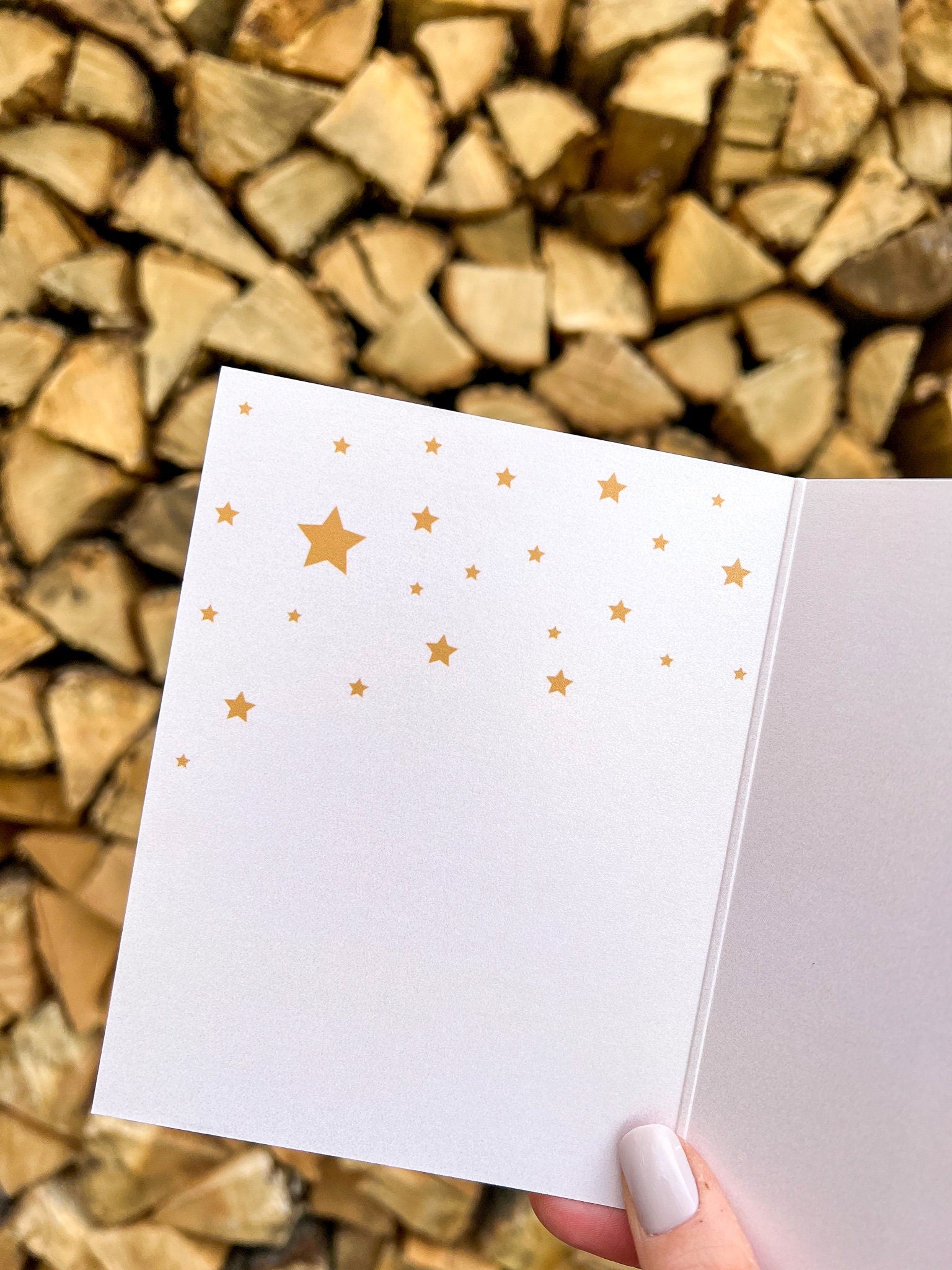 A hand holding a Christmas card with 'Peace on Earth' written on it, featuring a green background, a red bow, and stars.