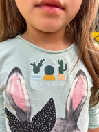 A clear sticker with a pun related to cacti, held against a backdrop of green cacti. The sticker features an illustration of a cactus with the text 'LOOKIN' SHARP'.